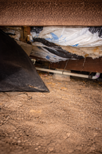 Damaged mobile home underbelly with exposed insulation and torn belly board before manufactured home vapor barrier repair.